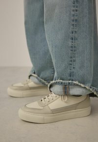 Baskets en cuir blanc à finition texturée, avec une bande accent grise. Associées à un jean bleu clair à ourlet effiloché.