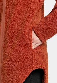 Ruskosexual fleece takki, jossa on pehmeä, teksturoitu kangas, vinoilla taskuilla ja rento malli, jossa on korkea-alhaallinen helma.