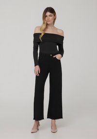 Body a maniche lunghe nera, scollata sulle spalle, abbinato a jeans neri a vita alta con gambe ampie, rifiniti con orli sfilacciati e tacchi a stiletto beige.