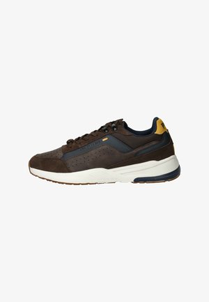 Bruine suède sneakers met marineblauwe accenten, voorzien van perforaties op de neus, een witte tussenzool en zwarte veters. Gele hielentab voegt detail toe.