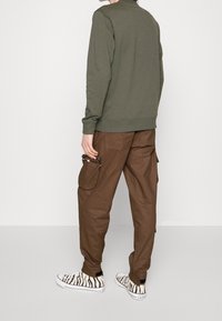 Groene sweatshirt, bruine cargobroek met zijzakken en zwart-witte sneakers met zebra-patroon. Eenvoudige, casual outfit gezien van de achterkant.