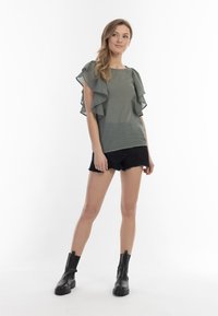 Grøn linned top med flæseærmer, parret med sorte slidte denimshorts og sorte ankelstøvler. Minimalistisk design med gennemsigtige accenter.