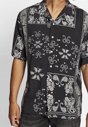 Chemise noire à manches courtes boutonnée avec motifs bandana blancs de style paisley et floraux portée par une personne du cou aux hanches.