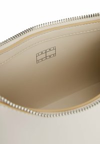 Wnętrze beżowej skórzanej torby o gładkiej fakturze, z srebrnym zamkiem błyskawicznym i wytłoczonym logo "TOMMY JEANS" na jasnym tle.