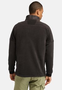 Pullover in pile nero con collo alto, caratterizzato da un pannello posteriore testurizzato e polsini a costine. Il tessuto appare morbido e caldo.