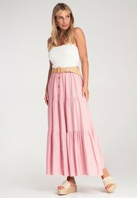 Helle rosa Maxikleid mit gestuftem Design und Knöpfen vorne, kombiniert mit einem strukturierten beigen Gürtel. Getragen mit Plateausandalen.