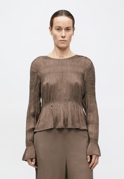 Barna peplum blúz hosszú ujjakkal, redős mintázattal, ráncolt részletekkel és bővülő mandzsettákkal, könnyű, szaténhoz hasonló anyagból készült.