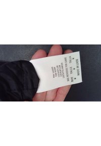 Černá nylonová tkanina s bílým štítkem péče, který uvádí obsah materiálu a velikost. Na štítku je napsáno: "100% nylon, velikost M, vyrobeno v Laosu."