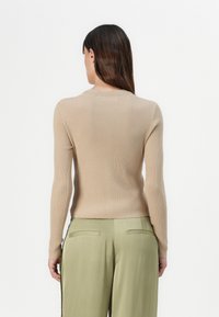 Beige geripptes Sweatshirt mit langen Ärmeln und Rundhalsausschnitt, kombiniert mit olivgrünen Hosen mit Seitentaschen und glatter Textur.