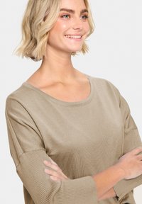 Maglione leggero beige in maglia con scollo rotondo e polsini a costine. Il tessuto ha una texture liscia e una vestibilità comoda con maniche a tre quarti.