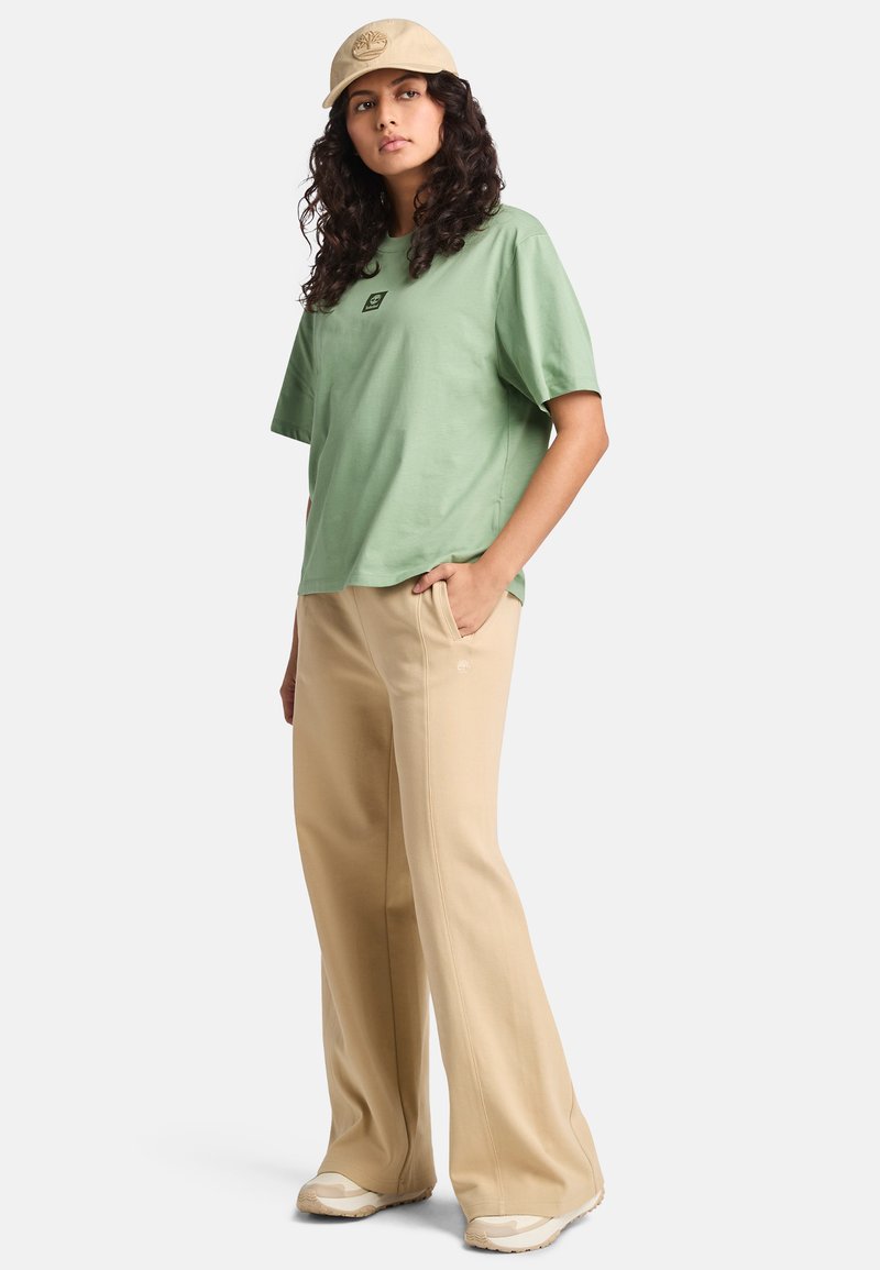 Light green cotton t-shirt with short sleeves and a logo. Beige, wide-leg pants with pockets. Light-colored shoes, simple design.