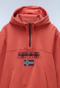 Felpa corallo con design a mezza zip, caratterizzata da un logo "NAPAPIJRI geographic" in nero e una patch della bandiera norvegese sul davanti. Texture liscia.