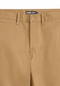 Bruna chinos med en traditionell passform, utrustade med dragkedja, knappstängning och bälteshällor. Etiketten säger "Vans Authentic Chino."