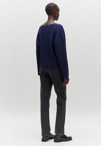 Marineblauer gerippter Strickpullover mit lässigen Schultern, kombiniert mit grauen schmal geschnittenen Jeans. Das Outfit zeichnet sich durch eine entspannte Silhouette und minimalen Zubehör aus.