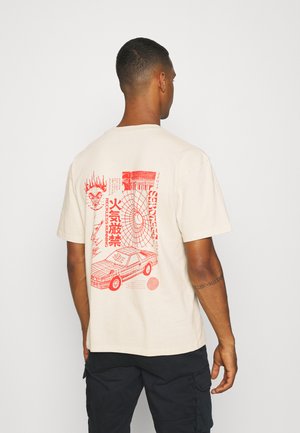 T-shirt en coton beige avec un grand imprimé graphique rouge au dos, représentant une voiture, un design circulaire et des accents de texte. Manches courtes.