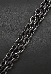 Black leather background with two linked metal chains in a shiny, dark finish, showcasing rounded links with a smooth texture.