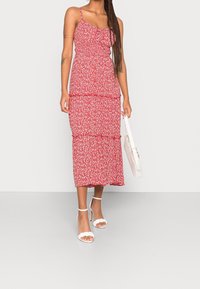 Röd midi-klänning med blommönster, tunna axelband, resår på överdelen och kjol i flera lager. Matchas med vita klackade sandaler och en liten vit handväska.