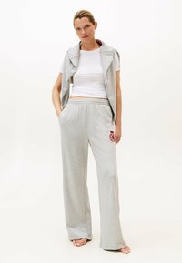 Grijze sweatpants met een elastische tailleband en zijzakken, gecombineerd met een wit aansluitend t-shirt en een grijze mouwloze hoodie.