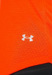Klart orange atletisk tyg med ett texturerat mönster och små perforeringar, accentuerat av en vit Under Armour-logotyp. Svart kant längst ner.