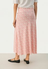 Gonna midi rosa con motivo floreale, realizzata in tessuto morbido, con una forma fluida che si adagia a terra. Scarpe nere flat completano l'outfit.