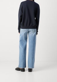 Granatowy sweter z luźnym krojem, zestawiony z jasnoniebieskimi spodniami typu wide-leg. Czarny obuwie na słupku dopełnia całość.