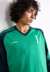 Green sports jersey with long navy sleeves, featuring a v-neck, white number "1," and adidas logo in white. Textured fabric with stripes.