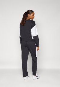 Fato de treino preto e branco com um design de blocos de cor. O sweatshirt apresenta um decote redondo e punhos em ribana; as calças têm um corte afunilado com riscas laterais.