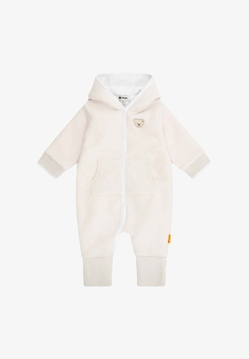 Combinaison beige avec une fermeture éclair blanche, une capuche et un patch d'ours. Comprend une poche avant et des poignets à côtes. Texture douce, semblable à de la polaire.
