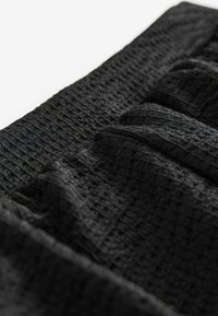 Zwart textiel met een gekreukt ontwerp en horizontale plooien. Het oppervlak heeft een golvend patroon.