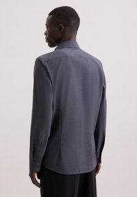Maglietta a maniche lunghe grigio scuro con tessuto texture, polsini con bottoni e colletto classico, che mostra una vestibilità su misura e linee pulite.