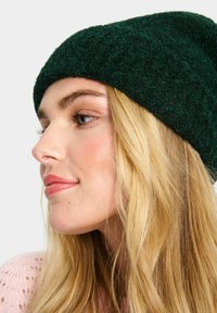 Green knitted beanie with a textured, fuzzy surface. The design is slouchy, fitting snugly at the forehead and casual in shape.
