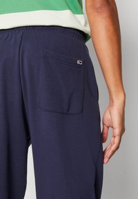 Marinblåa träningsoverallsbyxor med en sidoficka som har ett kontrasterande logotypmärke. Tillverkade av mjukt tyg, med en elastisk midja för komfort.