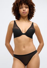 Juodas apatinis trikotažas, susidedantis iš permatomų liemenėlės su metaliniais kaušeliais ir atitinkamų žemai nuleistų kelnaičių. Minkšta medžiaga su plonais dirželiais ir logotipu dekoruota juosta.