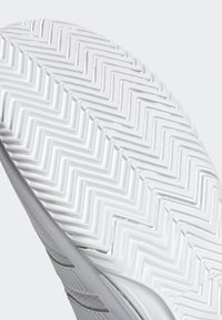 Podrážka topánky z bieleho gumového materiálu, s rybej kosťovej vzorom na behúni a hladkým povrchom, zobrazená pod uhlom na lepšiu viditeľnosť dizajnu a textúry.