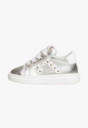 Niski sneaker ze srebrnej metalicznej skóry, białe sznurówki, białe ćwieki w kształcie serca ze złotymi akcentami oraz gruba biała gumowa podeszwa.