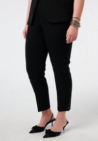 Zwarte, op maat gemaakte pantalon van glad materiaal met een slank ontwerp, voorzien van zijsplitjes bij de zoom en gecombineerd met zwarte pumps met een puntige neus.