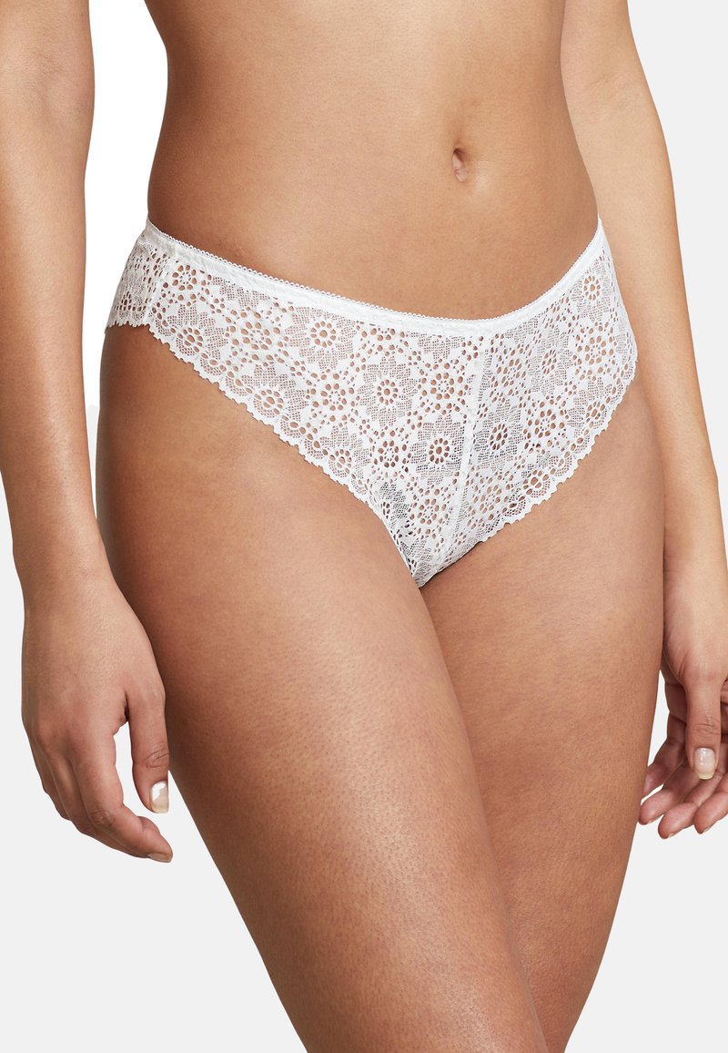 Witte kanten thong met bloemenpatroon, voorzien van een golvende rand rond de taille en benen. Zachte, semi-doorzichtige textuur, lage taille.