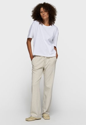 Maglietta bianca oversize a maniche corte abbinata a pantaloni della tuta beige chiaro con coulisse in vita e gambe larghe. Calzature casual incluse.