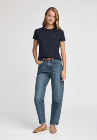 Granatowa bawełniana koszulka z krótkim rękawem i okrągłym dekoltem, sparowana z jasnoniebieskimi, wysokimi jeansami i beżowymi balerinami. Prosty design, swobodny krój.