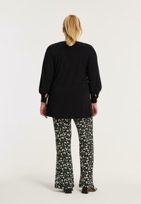 Zwarte longsleeve top met zijsplitten, gecombineerd met uitlopende broek met een bloemenpatroon op een donkere achtergrond.