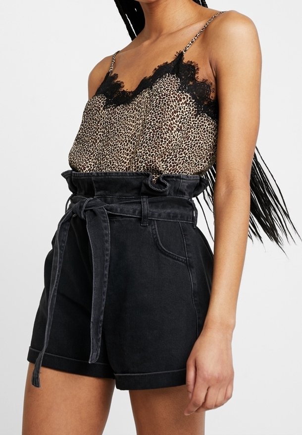 Femme portant un caraco imprimé léopard avec bordure en dentelle noire, rentré dans un short noir taille haute ceinturé en tissu.