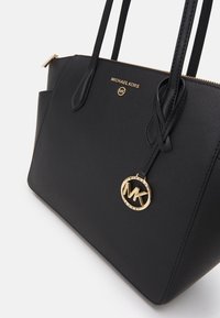 Zwarte leren tote bag met gouden hardware, voorzien van een logo charm en dubbele handvatten, een gladde textuur en een gestructureerde vorm.