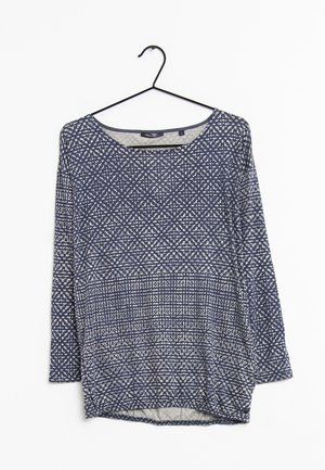 Chemise bleu marine à manches longues avec des motifs géométriques blancs en points, suspendue sur un cintre noir sur fond blanc.