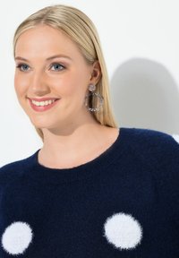 Námořnický svetr s bílými chlupatými puntíky, pletená textura, kulatý výstřih. Velké kulaté náušnice v transparentních a bledě růžových tónech.