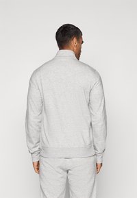 Light gray sweatshirt with a high collar, ribbed cuffs, and hem. Material appears soft and textured. Worn with matching gray sweatpants.