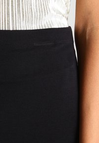 Jupe noire en stretch avec une texture lisse et une taille élastique, associée à un haut clair à rayures verticales.