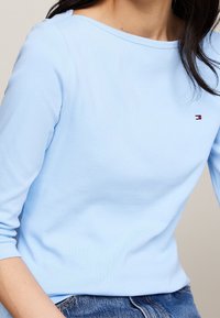 Maglia a maniche lunghe azzurro chiaro con scollatura a barca. Presenta un piccolo logo sul petto; realizzata in tessuto morbido e liscio con una vestibilità aderente.