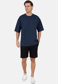 Oversized donkerblauw t-shirt met korte mouwen, gecombineerd met zwarte shorts en witte sneakers. Eenvoudig en casual ontwerp met minimale details.