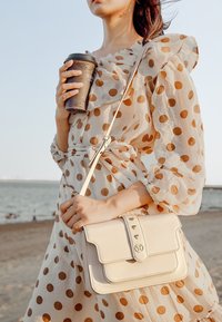 Borsa in pelle crema con chiusura a pattina, dettagli in hardware dorato e tracolla removibile. La borsa presenta una texture liscia e un design minimalista.