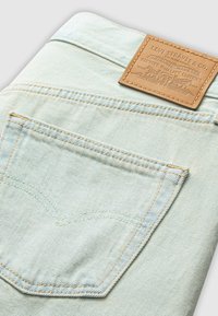 Světle modré džíny z denimu s viditelnou zadní kapsou s vyztuženým švem a hnědou koženou nášivkou na pásku s logem značky.